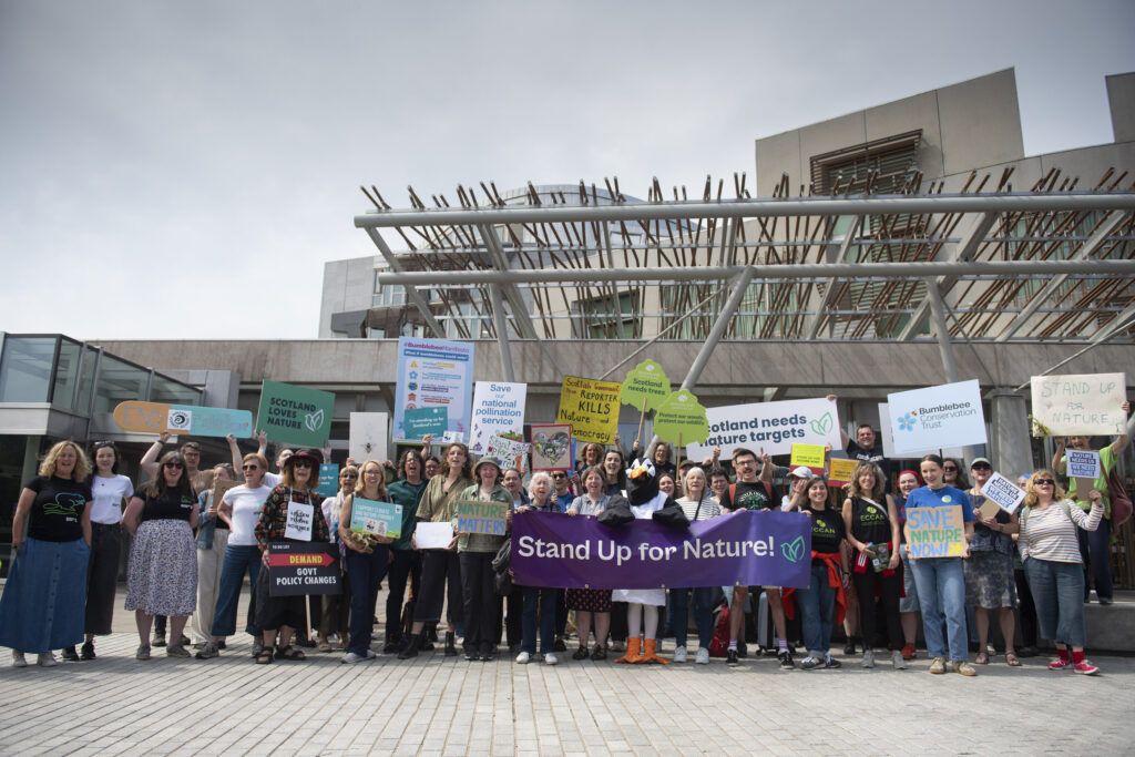 A group of people outside the Scottish Parliament holding signs which say Stand Up for Nature!
