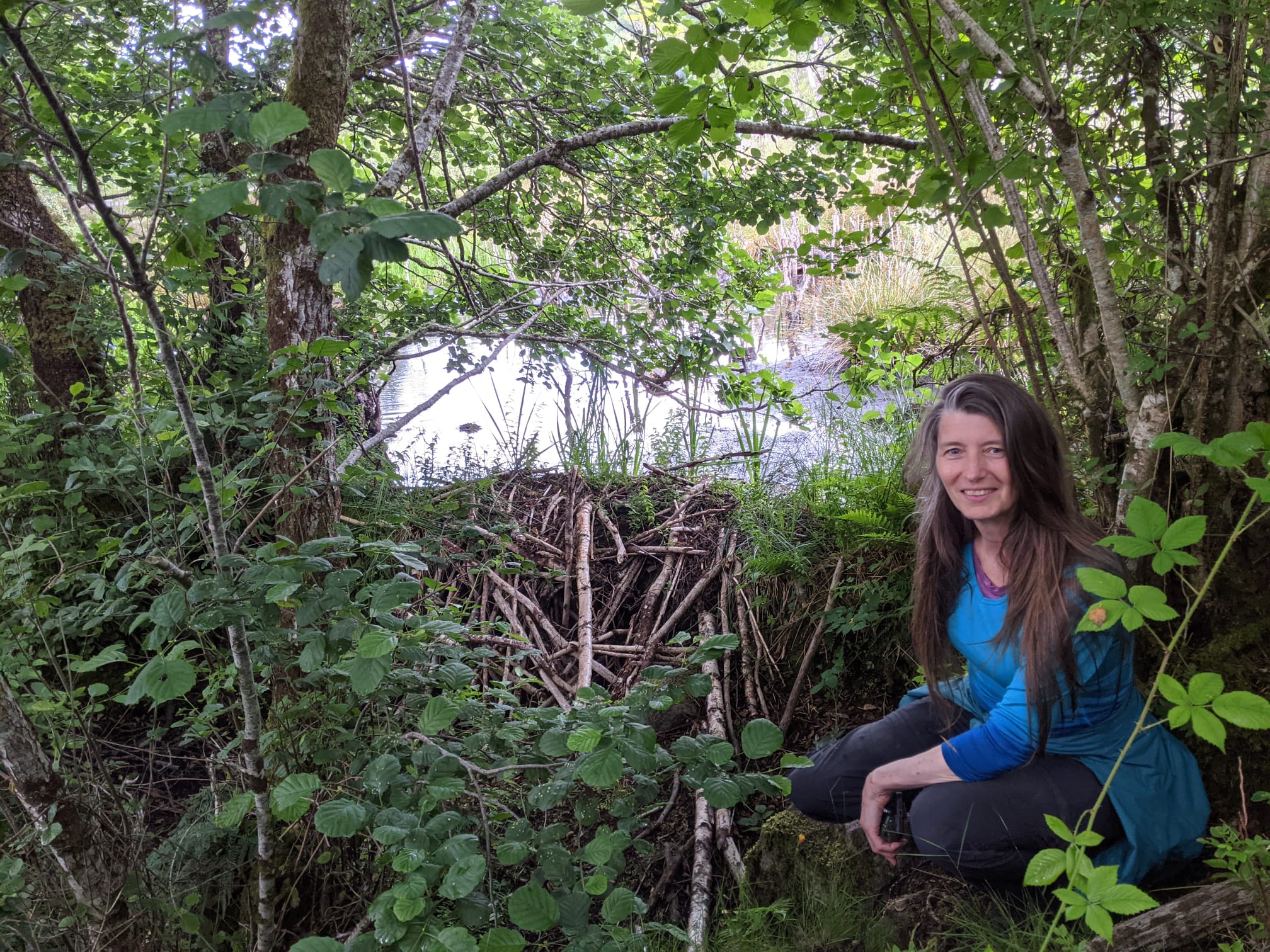 A woman sitting in front of a loch in the woods